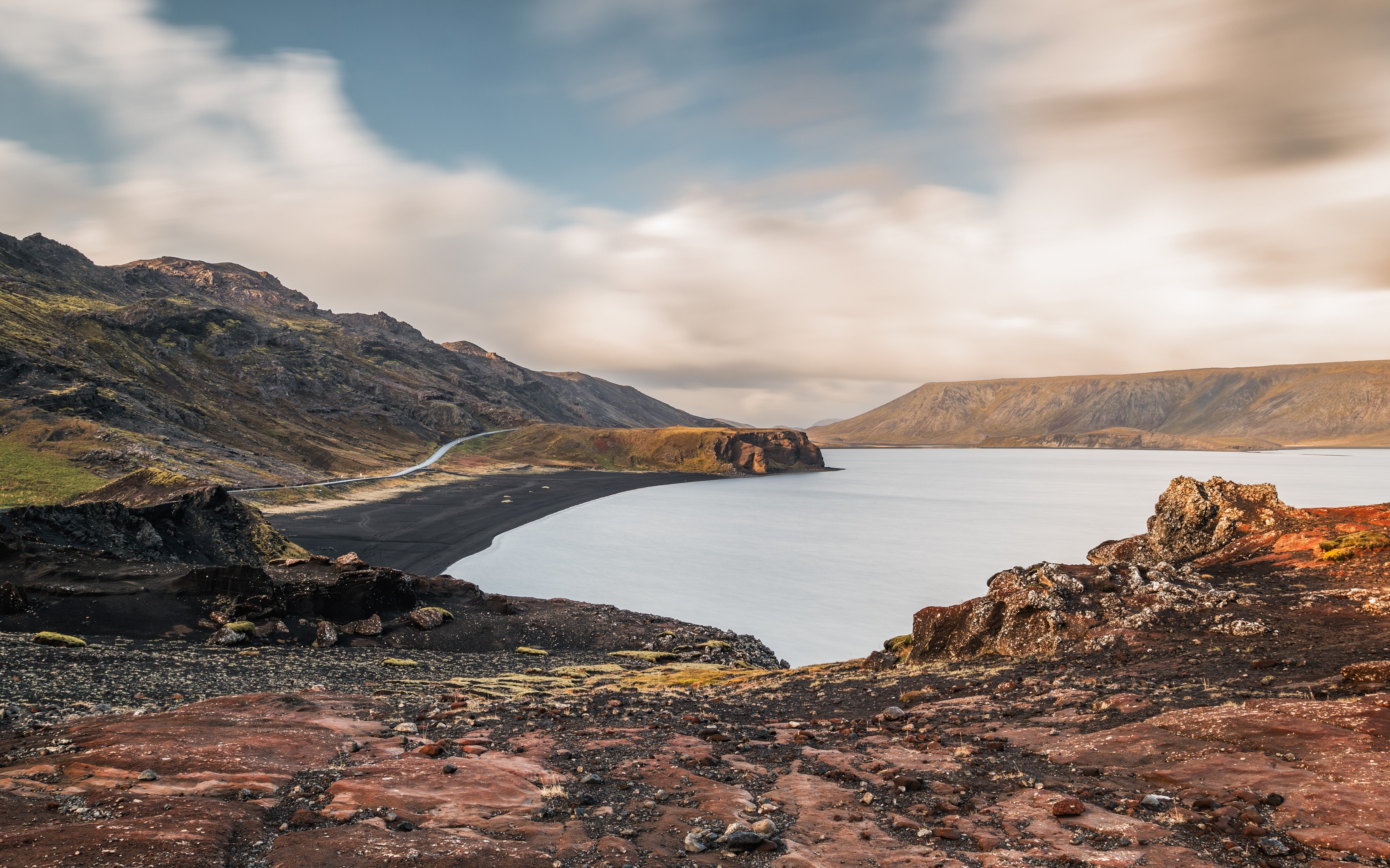 Scenic view of Lake Kleifarvatn with black sand beach, rugged cliffs, and a winding road on the Reykjanes Peninsula.