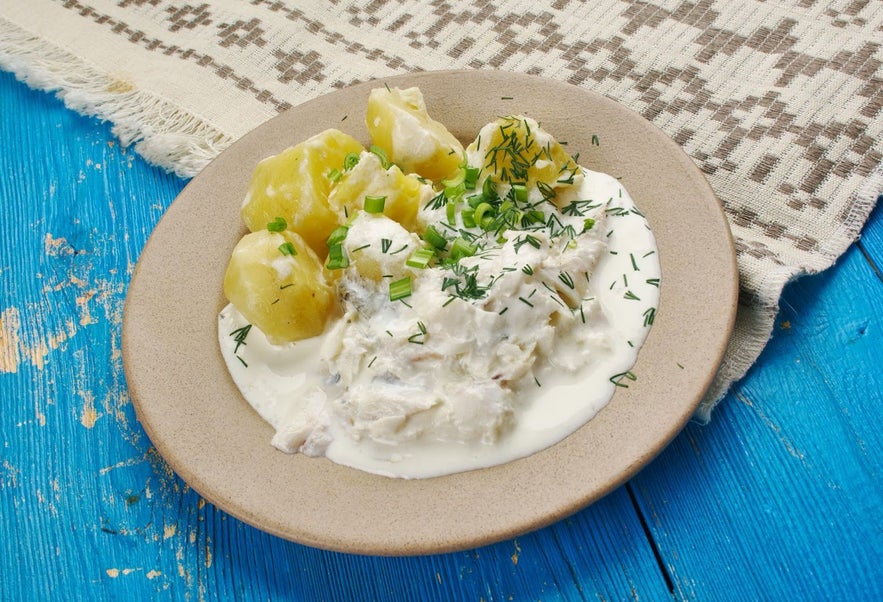 Traditional Icelandic fish stew with boiled potatoes, creamy white sauce, and fresh herbs on a beige plate.