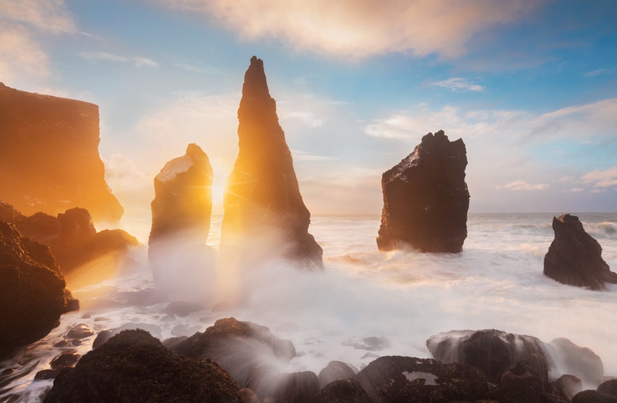 Sunset illuminating sea stacks and crashing waves at Reykjanes cliffs.