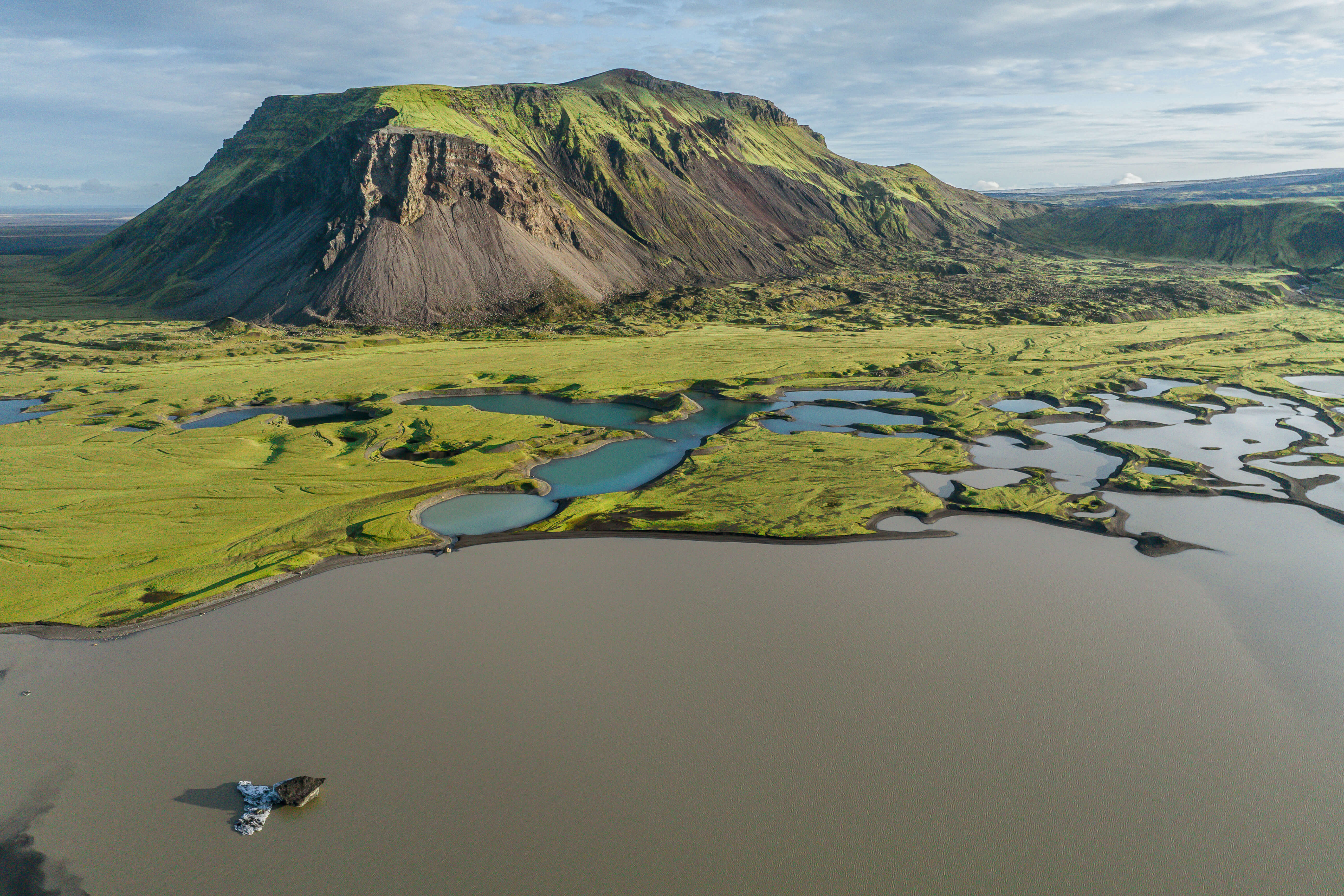Aerial view of mossy highland terrain and volcanic hill near Vik, with glacial lakes and braided river patterns.