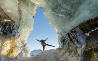 Traveler celebrating between sparkling ice walls at Katla Ice Cave.