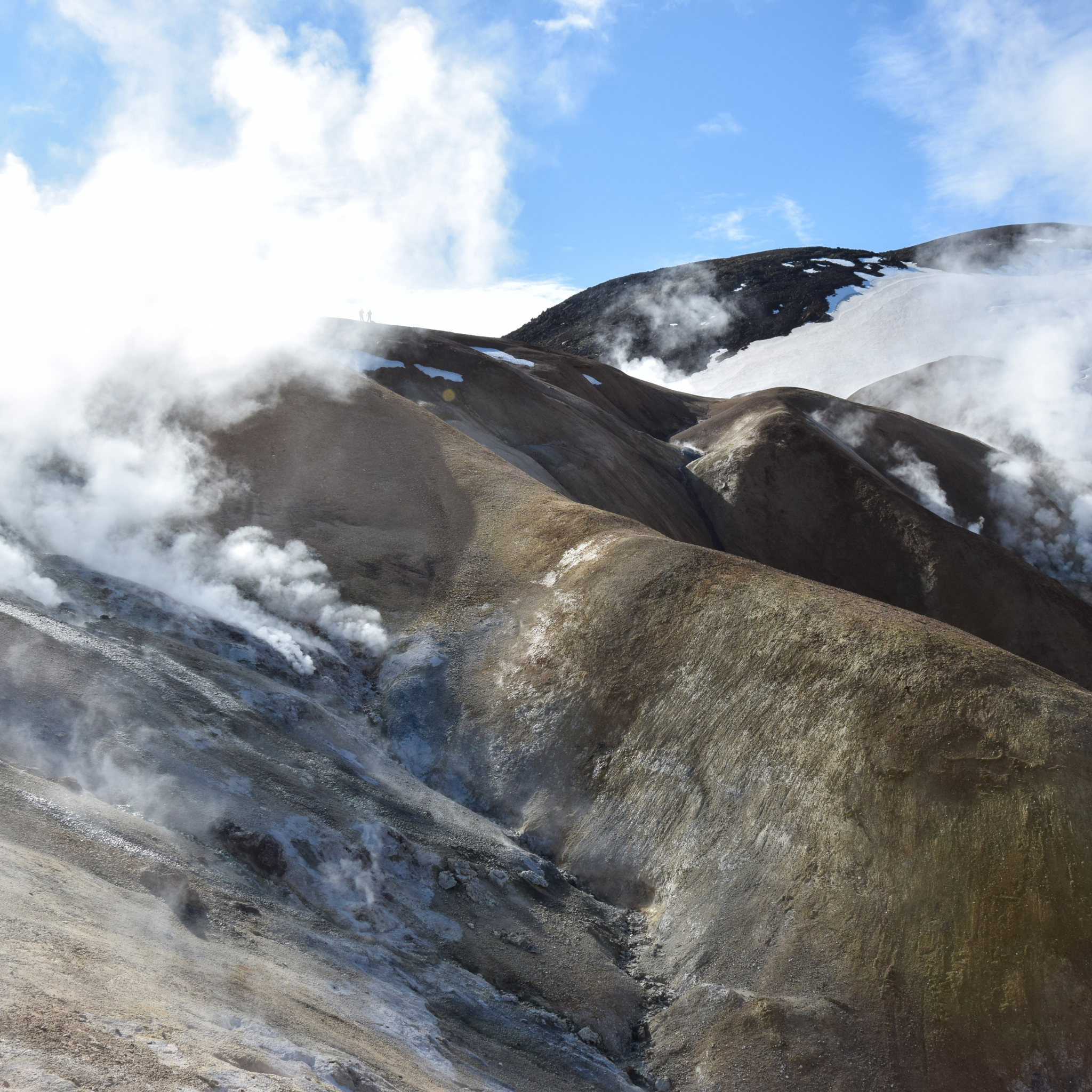 Steam rises from the geothermal hills of Hveradalir under a bright blue summer sky in Kerlingarfjoll, Iceland.
