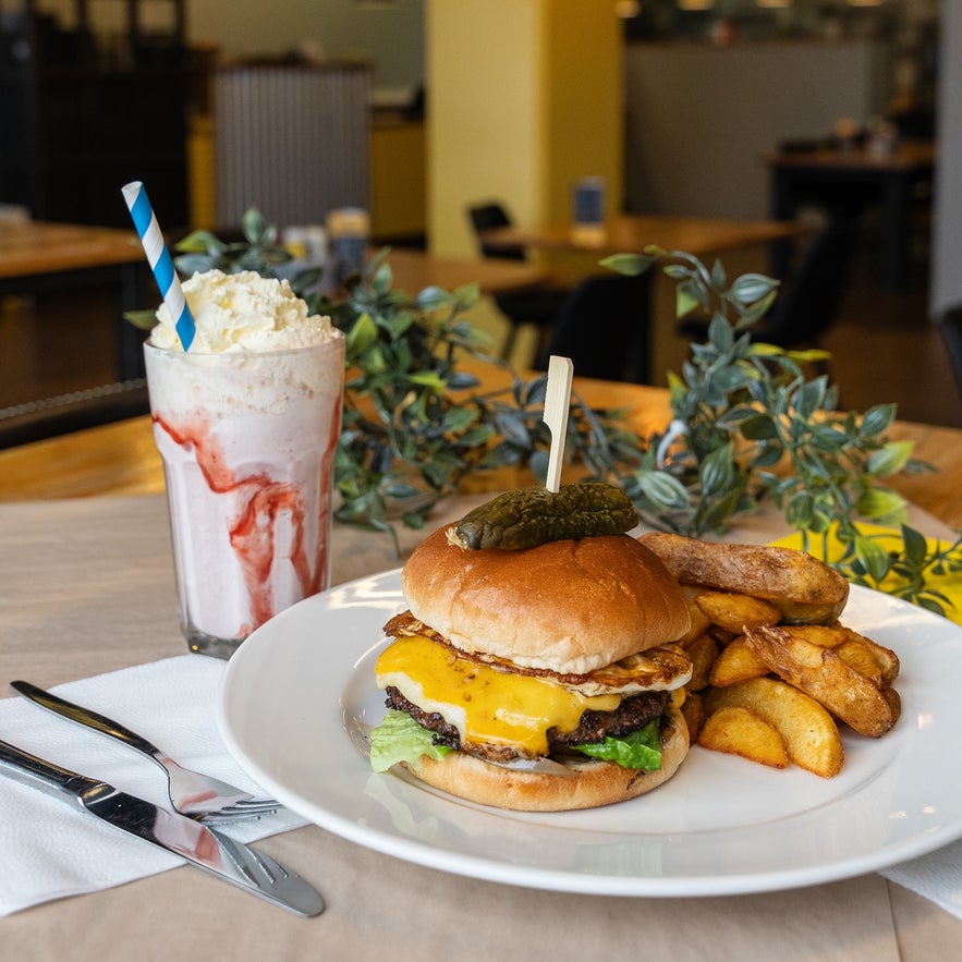 Cheeseburger gourmand avec frites, œuf et milkshake à la fraise, servi chez Byrja à Selfoss. Cheeseburger gourmand avec frites, œuf et milkshake à la fraise, servi chez Byrja à Selfoss.