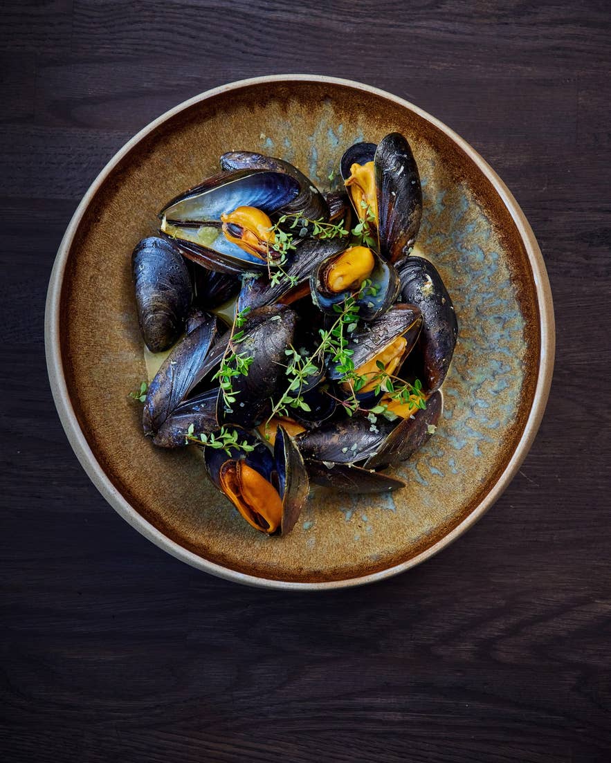A rustic brown plate filled with steamed mussels garnished with fresh thyme sprigs. A rustic brown plate filled with steamed mussels garnished with fresh thyme sprigs.
