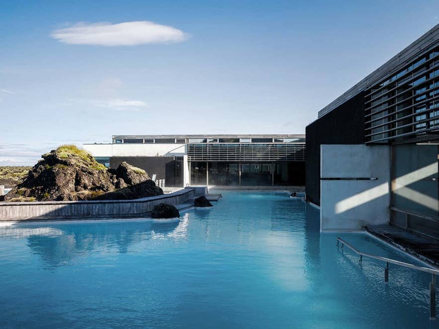 Silica Hotel van de geothermische spa Blue Lagoon in IJsland met melkblauw water, vulkanisch lavagesteente en opstijgende stoom onder een heldere hemel.