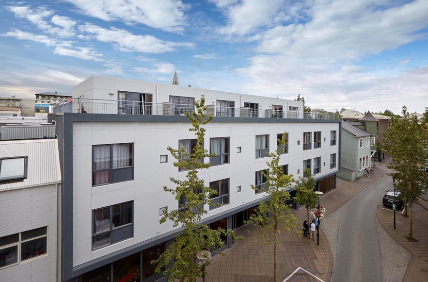 Modern exterior of Alda Hotel in Reykjavik, Iceland, located on Laugavegur street with tree-lined sidewalks and views of Hallgrimskirkja in the background.