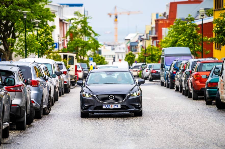 Auto che percorre una colorata via di Reykjavik fiancheggiata da auto parcheggiate e case islandesi