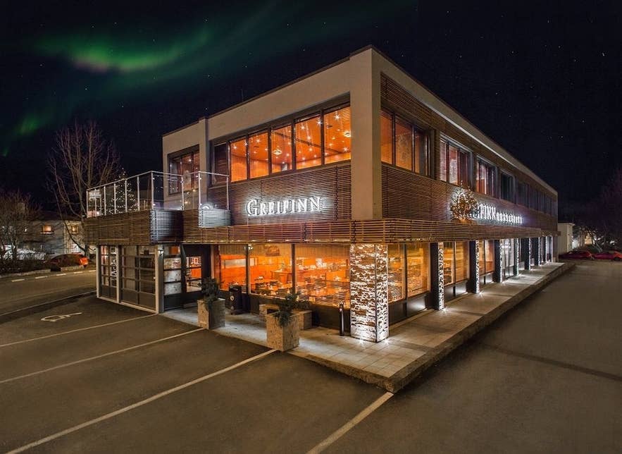 Greifinn Restaurant in Akureyri lit up at night with a cozy glow under the northern lights.
