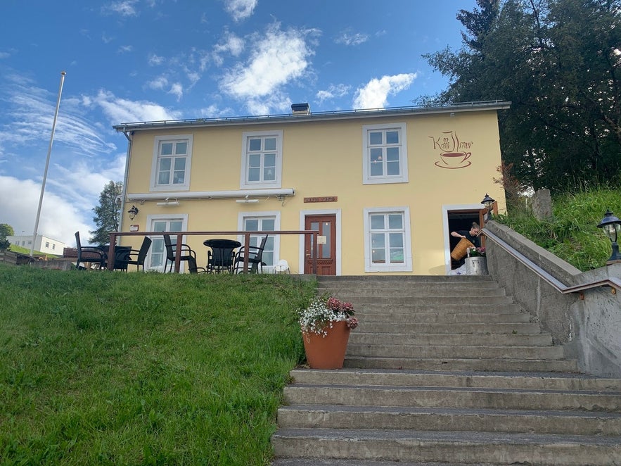 Kaffi Ilmur Breakfast Cafe in Akureyri features a homey facade, patio tables, and lush green surroundings.