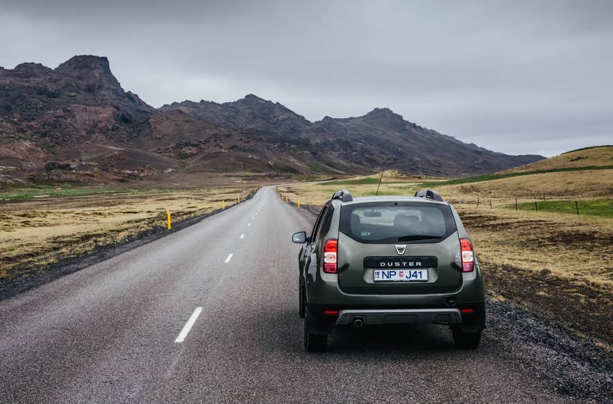 4x4 Dacia Duster op een lege weg door vulkanische bergen in IJsland, ideaal voor schilderachtige self-drive tours en een avontuur over de Ringweg