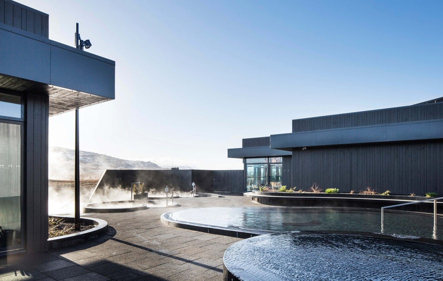 Krauma Spa i Borgarnes, Island, med dampende geotermiske bassiner, mørke bygninger og udsigt til bjergene under en klar himmel. Krauma Spa i Borgarnes, Island, med dampende geotermiske bassiner, mørke bygninger og udsigt til bjergene under en klar himmel.