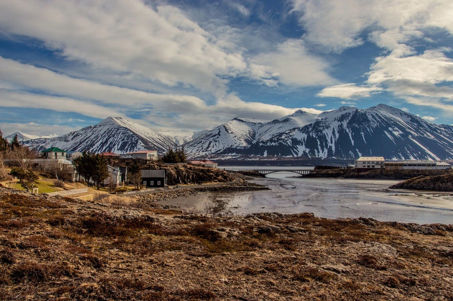 Scenic view of Borgarnes town with snow-capped Hlidafjall Mountain and bridge in West Iceland during spring.