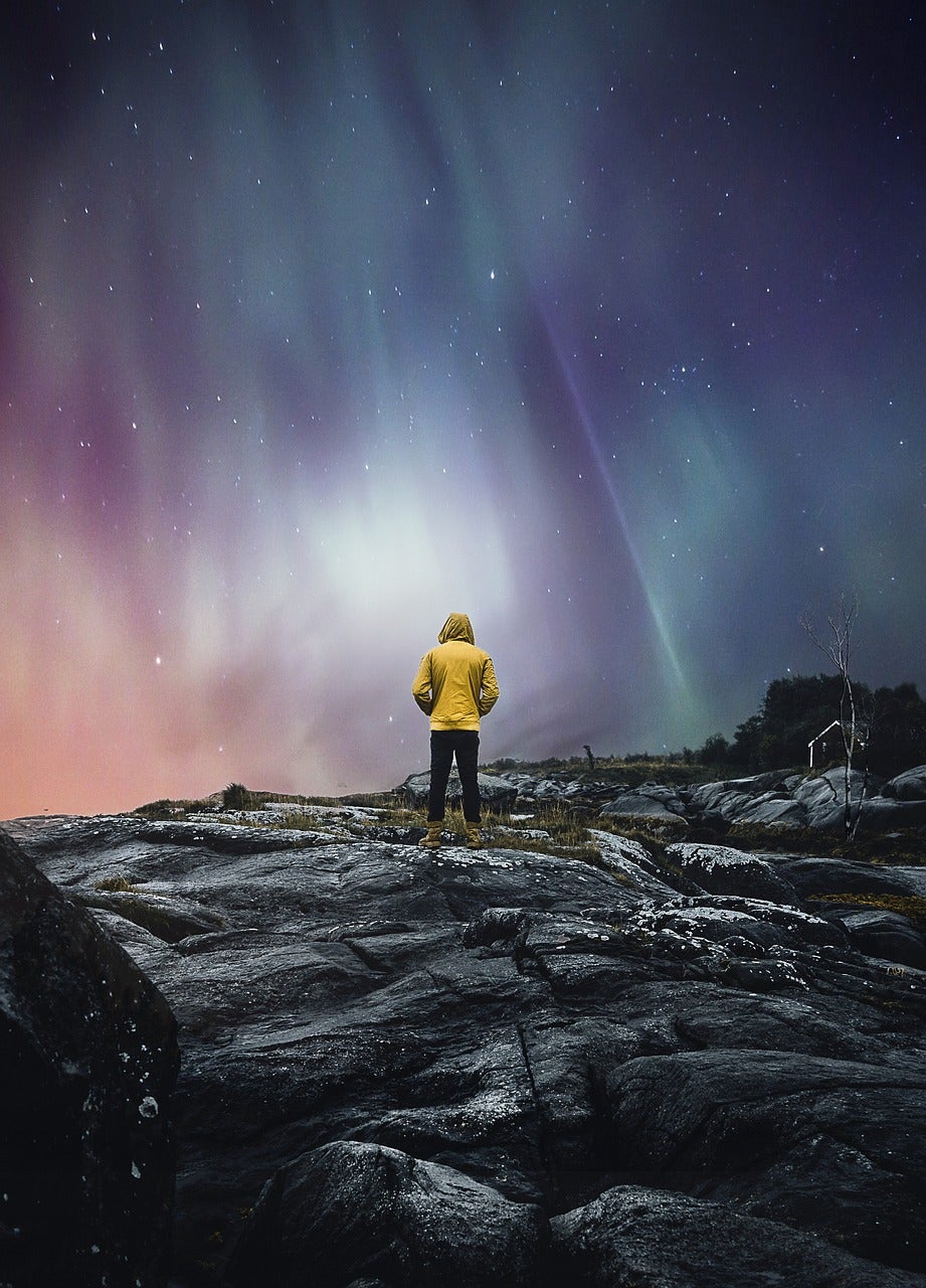 A solo person atop a rocky surface and under the northern lights.