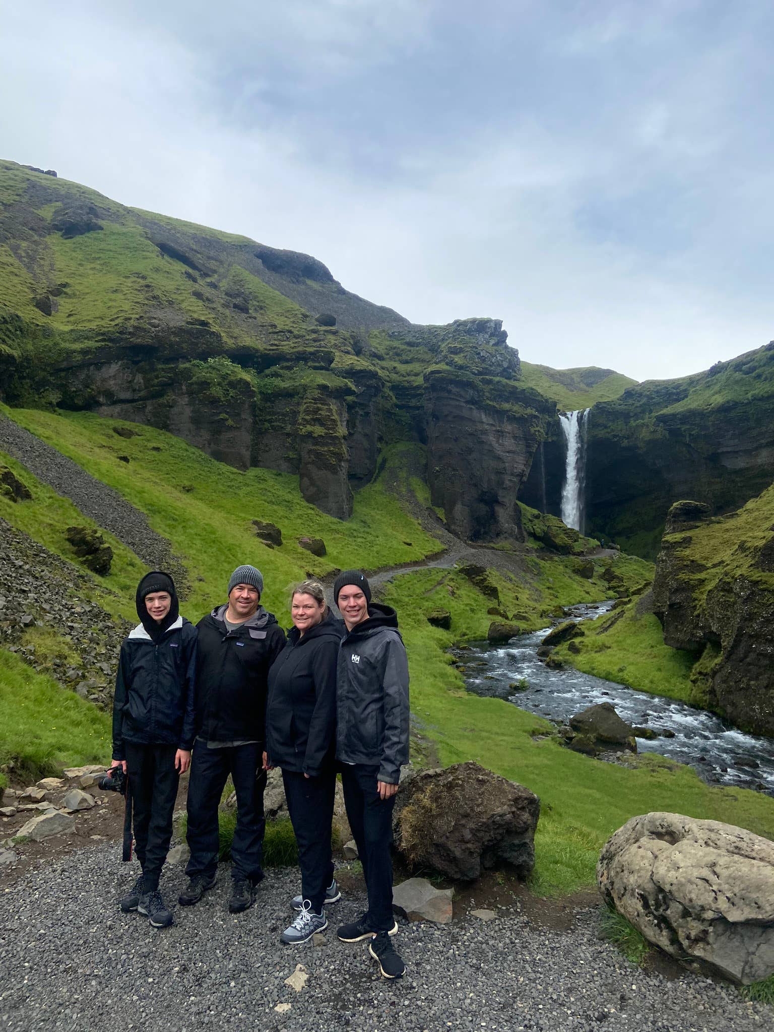 A group of tourists pose for a photo with a waterfall as their backgound on a South Coast tour.