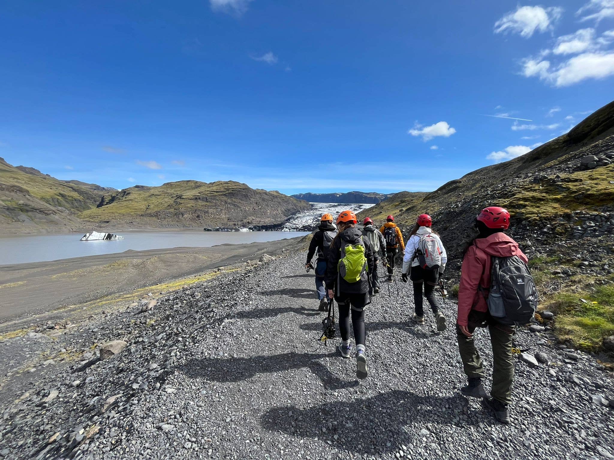 Group of hikers walking toward Solheimajokull Glacier under a bright sky.