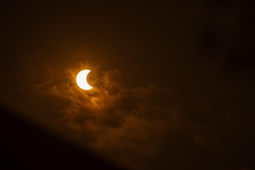 A partially eclipsed Sun glows through thin clouds in a dark sky during the early phase of a solar eclipse.