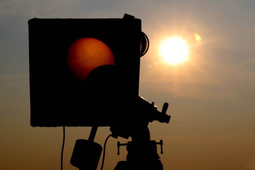 A solar eclipse camera with filters projects a partial eclipse onto a screen, with the Sun shining in the background.
