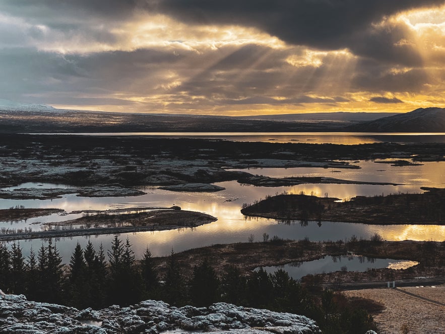 At sunrise in Thingvellir National Park in Iceland, Almannagja Gorge is visible with snow-covered ground, lakes, and clouds reflecting light along the Golden Circle route..