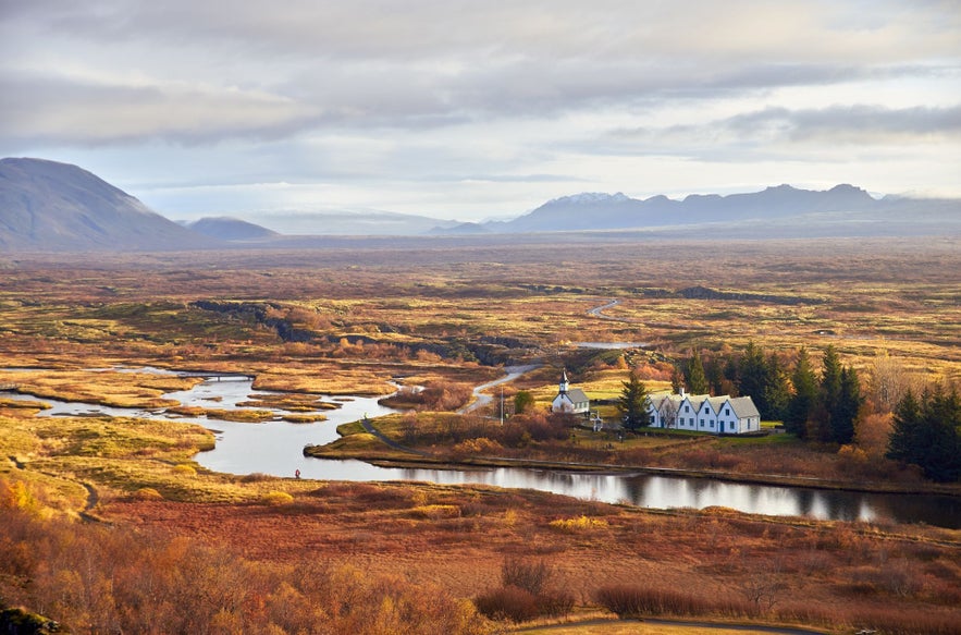 Thingvellir National Park in Iceland during autumn, with colorful foliage, winding river, historic church and buildings, distant mountains, and scenic landscape on the Golden Circle route.