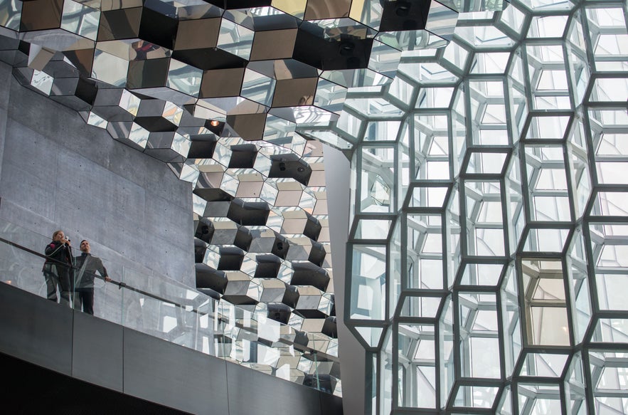 Interior of Harpa Concert Hall in Reykjavik, Iceland, with geometric glass facade, reflective ceiling panels, modern architecture, and visitors observing the design.