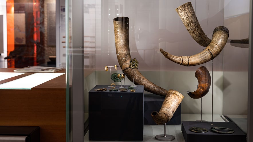 Viking artifacts at the National Museum of Iceland in Reykjavík, with carved drinking horns, jewelry, and ornaments displayed in a modern glass exhibit.