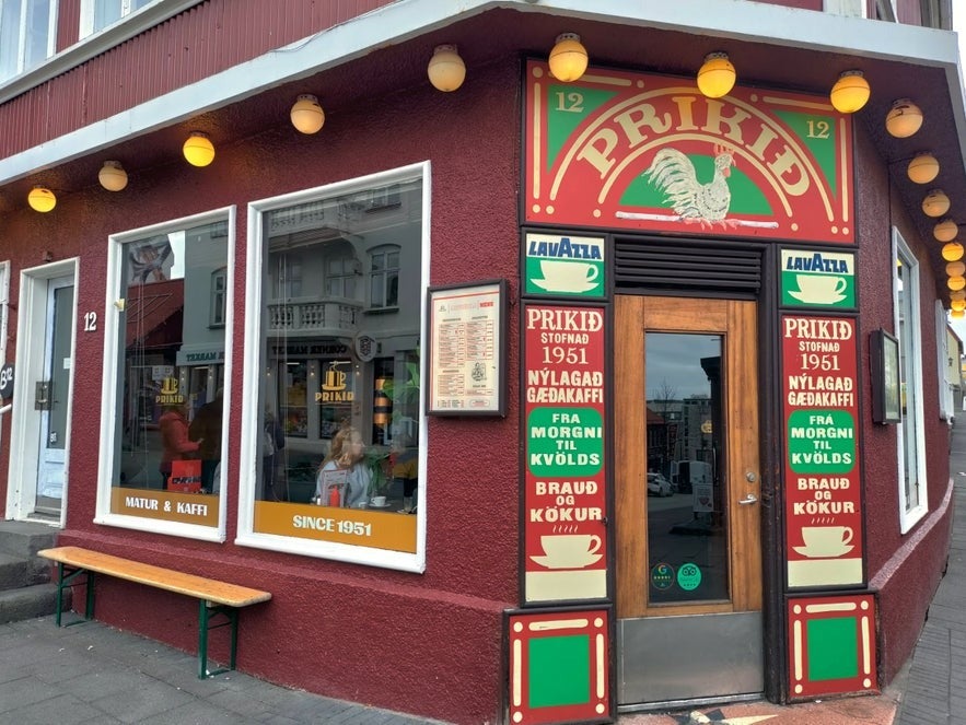 Exterior of Prikið café in Reykjavik, Iceland, with red facade, colorful vintage signage, street view, outdoor bench, and Lavazza coffee branding.