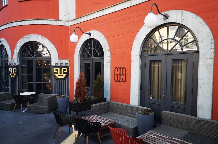 Outdoor terrace of the Grillmarket restaurant in Reykjavik, Iceland, with modern seating, orange facade, arched windows, and minimalist black and gold signage.