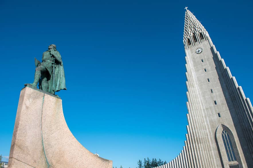 Hallgrimskirkja und Leif-Erikson-Statue in Reykjavik, Island, mit hohem Betonturm und klarem blauen Himmel an einem sonnigen Tag.