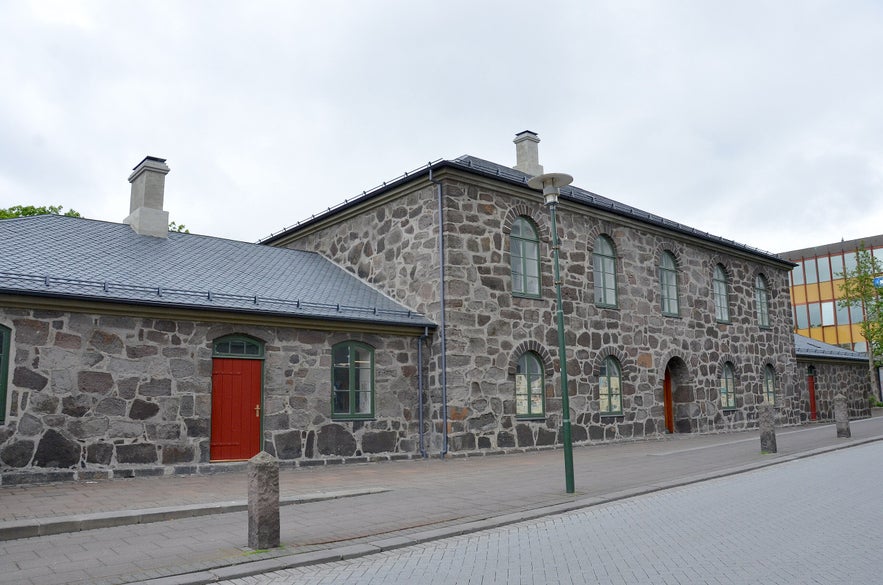 Hegningarhusid or Penalty House Prison in Reykjavik, Iceland, with grey stone facade, arched windows, and red doors by Skolavordustigur Street under cloudy sky.