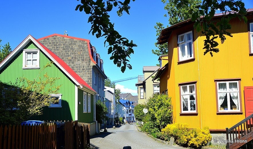 Grjotathorp neighborhood in Reykjavik, Iceland, with colorful historic wooden houses, green and yellow facades, narrow cobblestone street, trees, and bright summer sky.