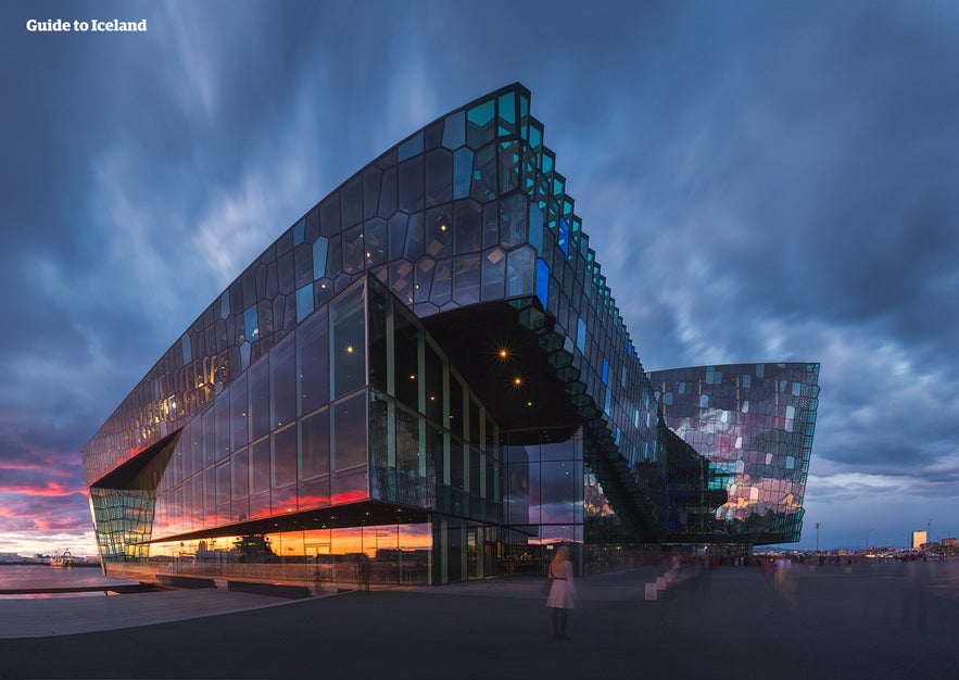 Harpa Concert Hall in Reykjavík, Iceland, at sunset with dramatic glass facade, colorful reflections, modern architecture, and illuminated evening sky.