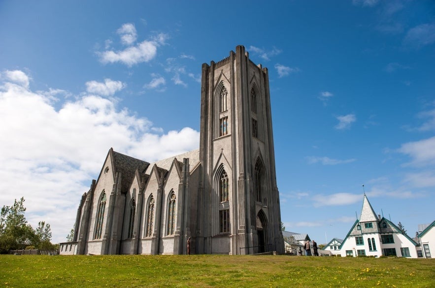Landakotskirkja cathedral in Reykjavik, Iceland, with tall grey concrete tower, gothic revival architecture, pointed arches, green lawn, and clear blue summer sky.