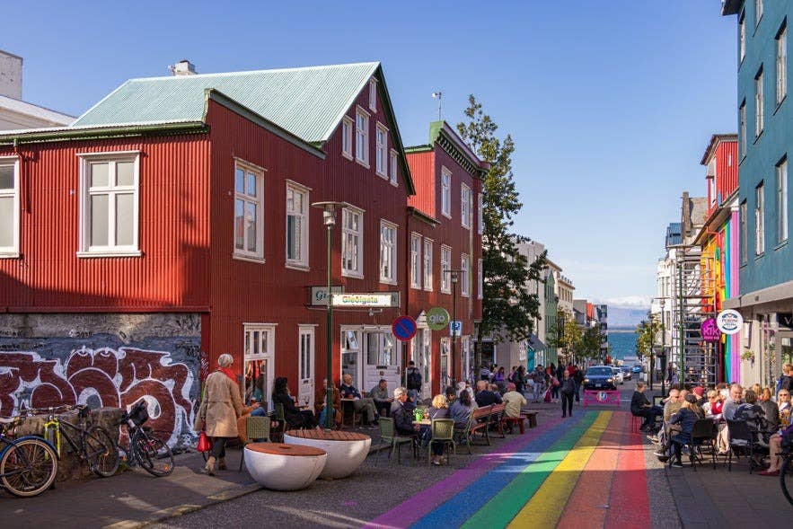 People sitting outside cafes on Reykjavik's rainbow street, with colorful buildings lining the road.