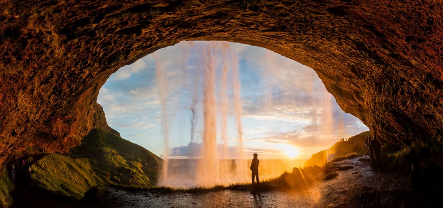 View from behind Seljalandsfoss waterfall at sunset in Iceland, showcasing golden light and scenic South Coast landscape