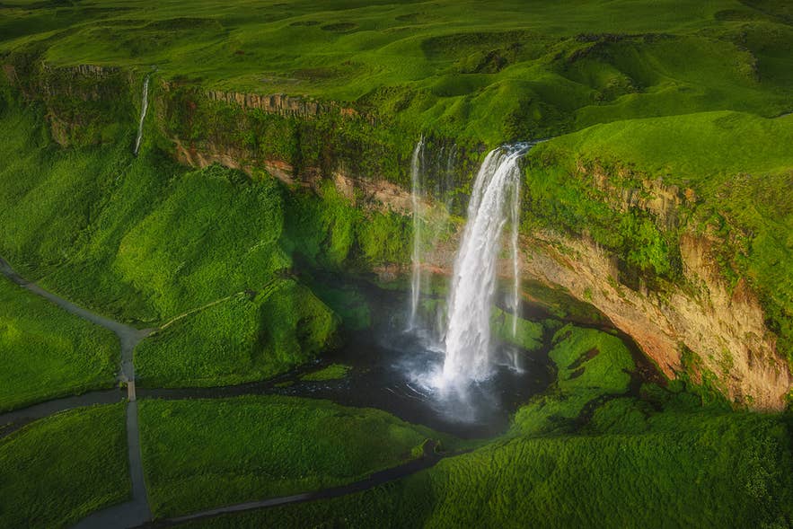 Luftfoto av Seljalandsfoss som stuper nedover grønne klipper på Islands sørkyst, sommerlandskap