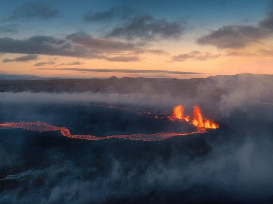 Vulkanische uitbarsting bij Sundhnukagigar in IJsland, met gloeiende lavafonteinen en een lavastroom bij zonsondergang in een indrukwekkend vulkaanlandschap