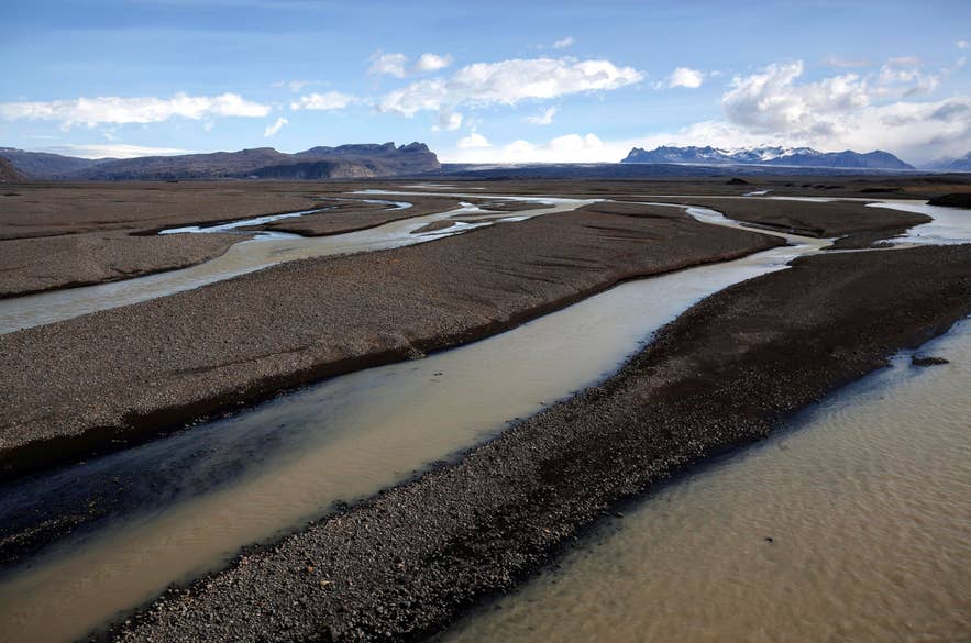 Die schwarze Sandebene Skeidararsandur im Süden Islands mit verzweigten Gletscherflüssen und ferner Bergkette unter strahlend blauem Himmel