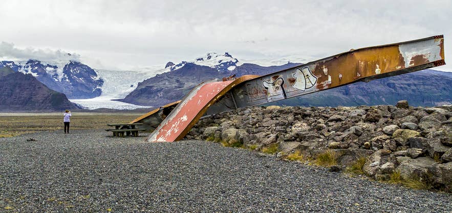 Überreste einer verdrehten Stahlbrücke, zerstört durch eine Gletscherflut (Jökulhlaup) nahe dem Skaftafell-Nationalpark mit dem Vatnajökull im Hintergrund.