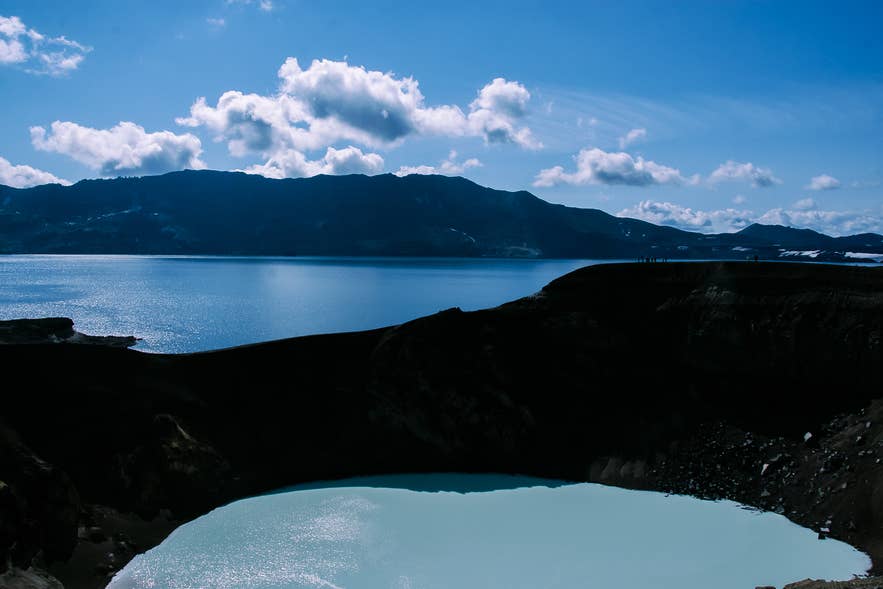 Askja volcanic caldera with turquoise Viti crater lake in the Icelandic Highlands, surrounded by dramatic mountain landscape under a bright summer sky.