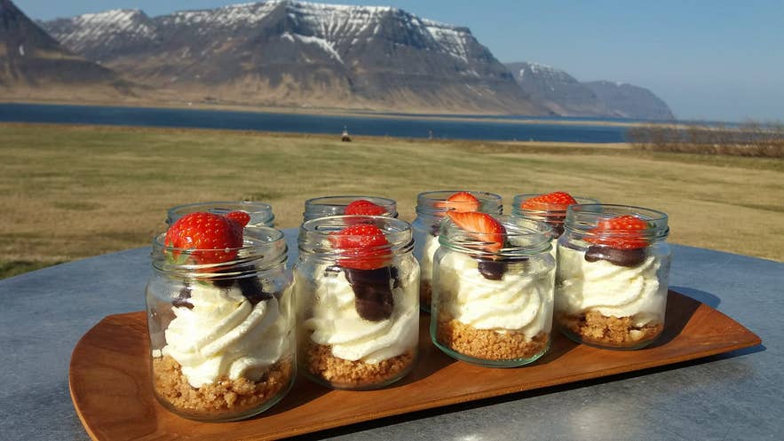 Eight jars of strawberry mousse cake with fjord and mountain views in the background at Kaffi Sol, Flateyri
