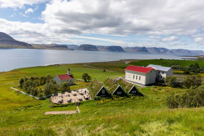 A distant view of Hrafnseyri's row of three black turf houses beside the Jon Sigurdsson Museum and a church