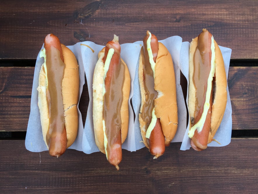 Close-up of Icelandic pylsur hot dogs with remoulade, brown mustard, and crispy onions, served with paper wraps at a Reykjavik hot dog stand.