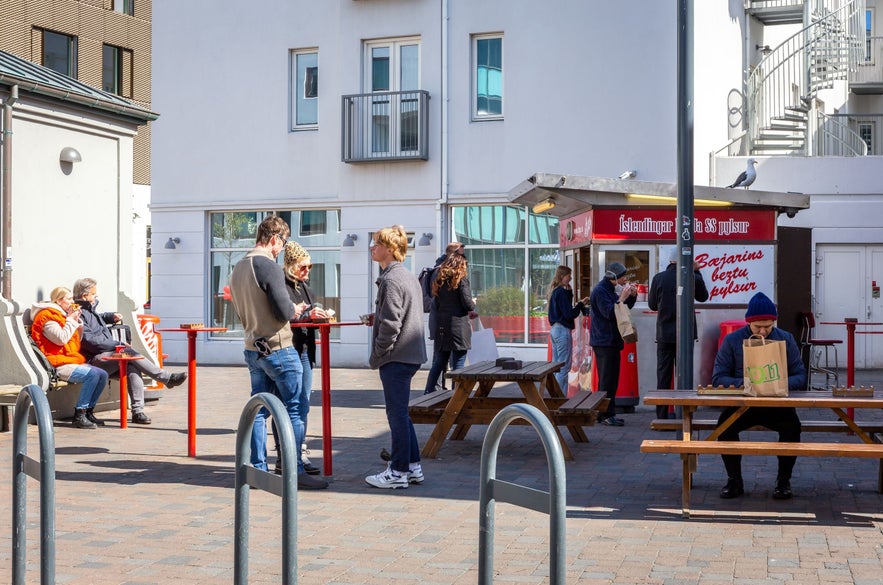 Tourists and locals enjoying Icelandic hot dogs at the famous Baejarins Beztu Pylsur stand in Reykjavik on a sunny day.