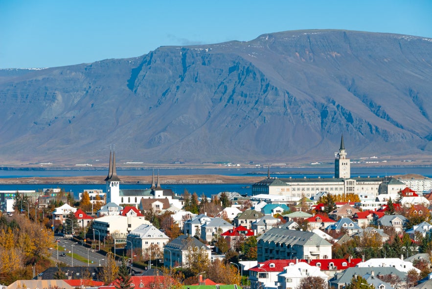Reykjavik cityscape in summer with colorful rooftops, church towers, and Mount Esja in the background under clear blue sky.