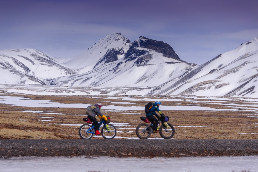 Two cyclists riding through snowy mountains in West Iceland
