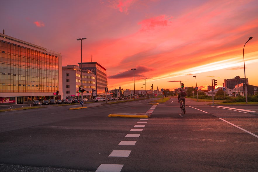 Cyclist riding through Reykjavik at sunset with city buildings and glowing sky.