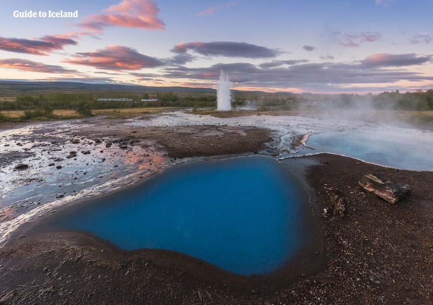 Strokkur geyser erupts in Geysir Geothermal Area, Iceland, with blue hot spring pool and colorful summer sunset sky. Strokkur geyser erupts in Geysir Geothermal Area, Iceland, with blue hot spring pool and colorful summer sunset sky.