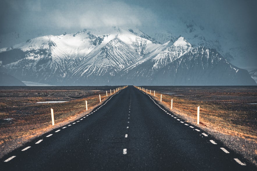 Iceland’s Ring Road stretching toward snow-covered mountains in moody weather.