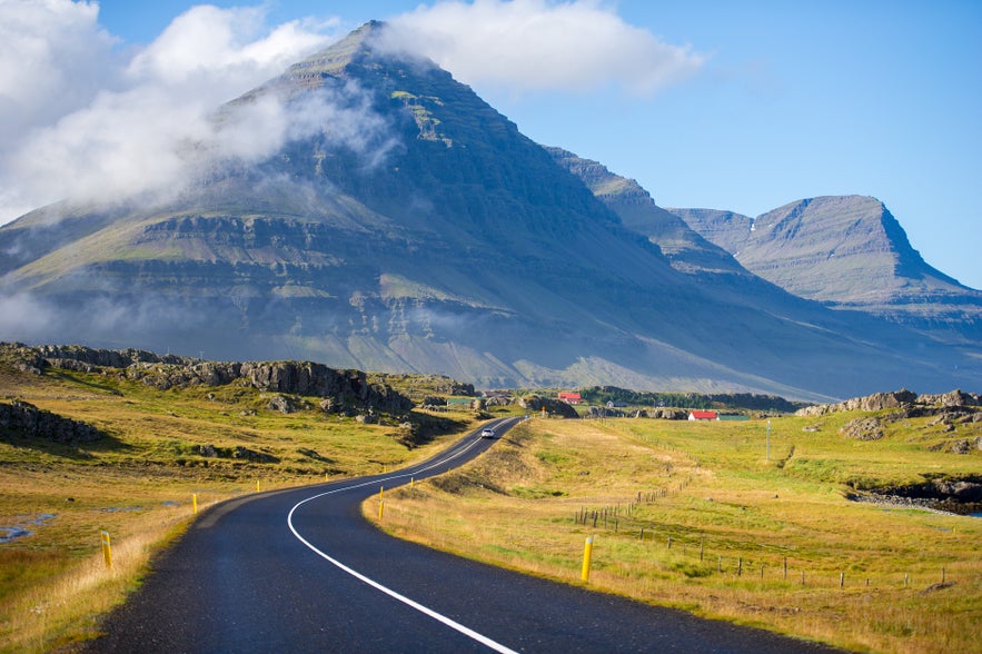 Iceland’s Ring Road (Route 1) winding through grassy fields with tall mountains in the background.