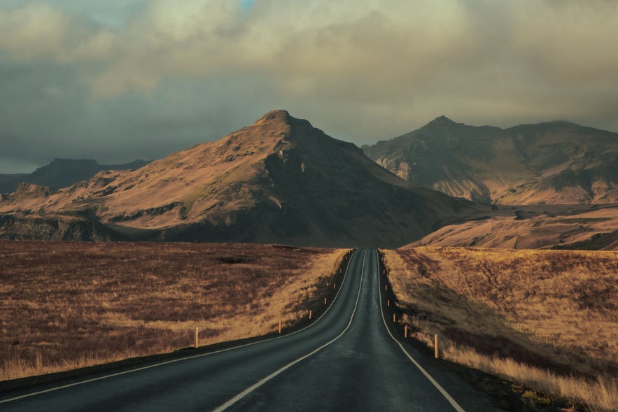 Golden Circle road in Iceland leading toward rugged mountains at sunset.